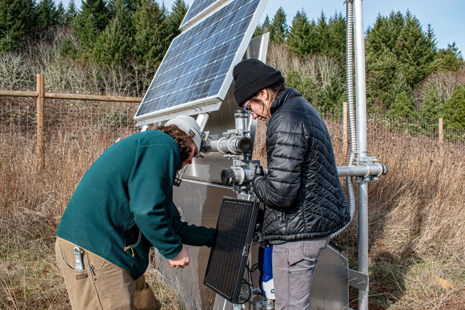 A young man and a young woman attach a sensor to a piece of seismic monitoring equipment.
